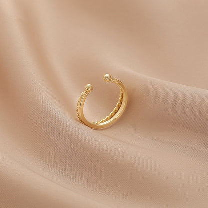 Elegant adjustable geometric double-layer gold ring with a twisted stripe design, crafted from premium copper, displayed on a soft aesthetic fabric background.