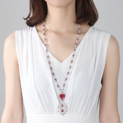 Elegant long crystal and ruby-toned statement necklace worn by a woman in a white dress, ideal for formal luxury fashion and evening events in the UAE.