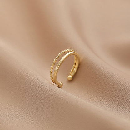 Elegant adjustable geometric double-layer gold ring with a twisted stripe design, crafted from premium copper, displayed on a soft aesthetic fabric background.